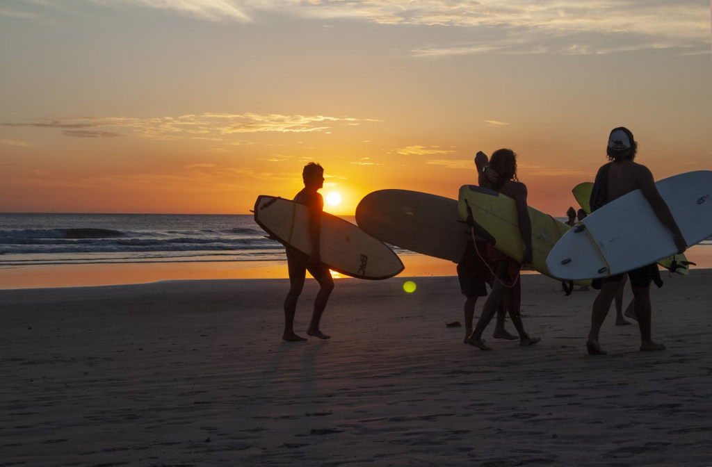 Group of people on the beach in Costa Rica at sunset holding surf boards after a day trip from Santa Teresa