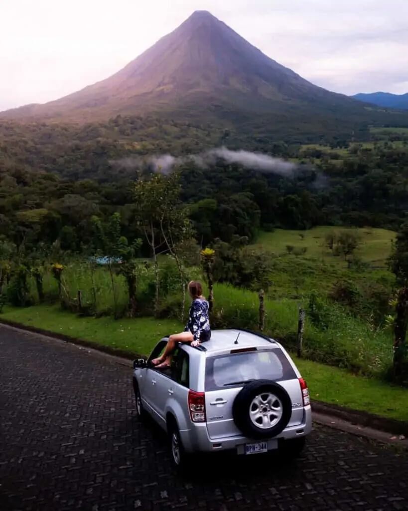 Woman sitting on car near tropical mountain