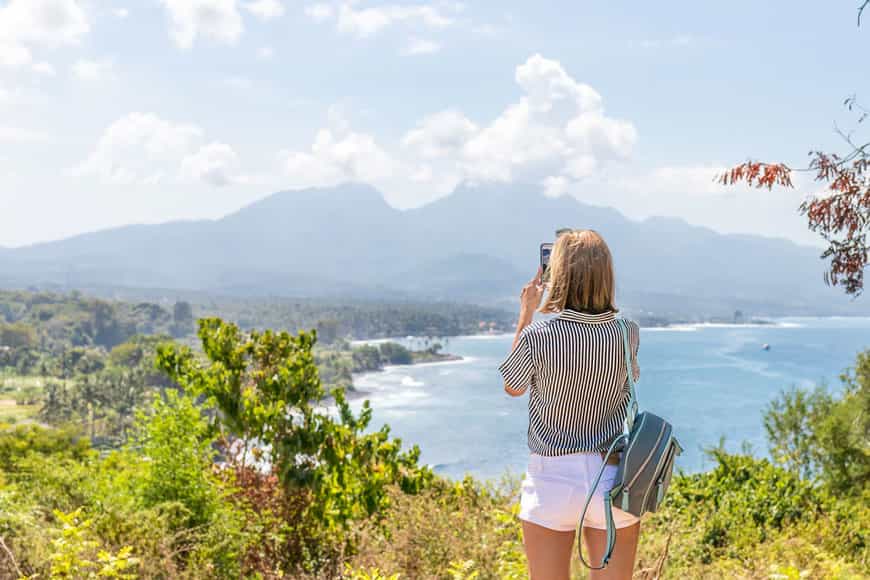 woman standing in front of beautiful beach scenery taking a picture