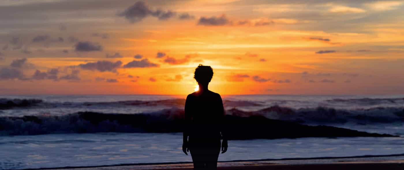 silhouetted woman in front of purple and orange sunset on beach