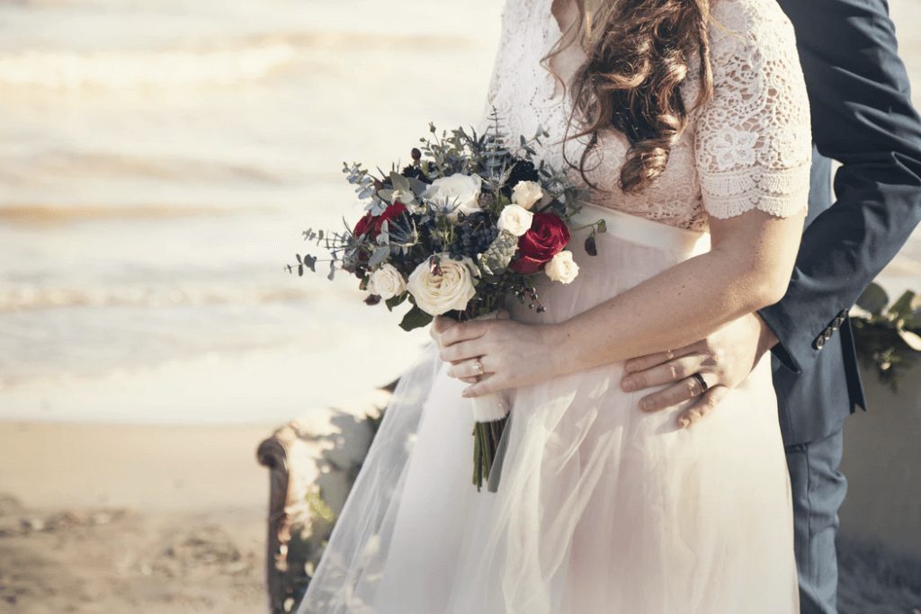 Bride and groom holding bouquet of roses on a beach