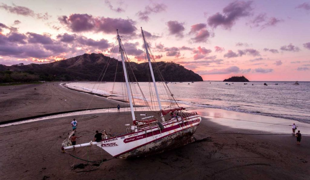 boat on a sandy beach in front of a pink and purple sky