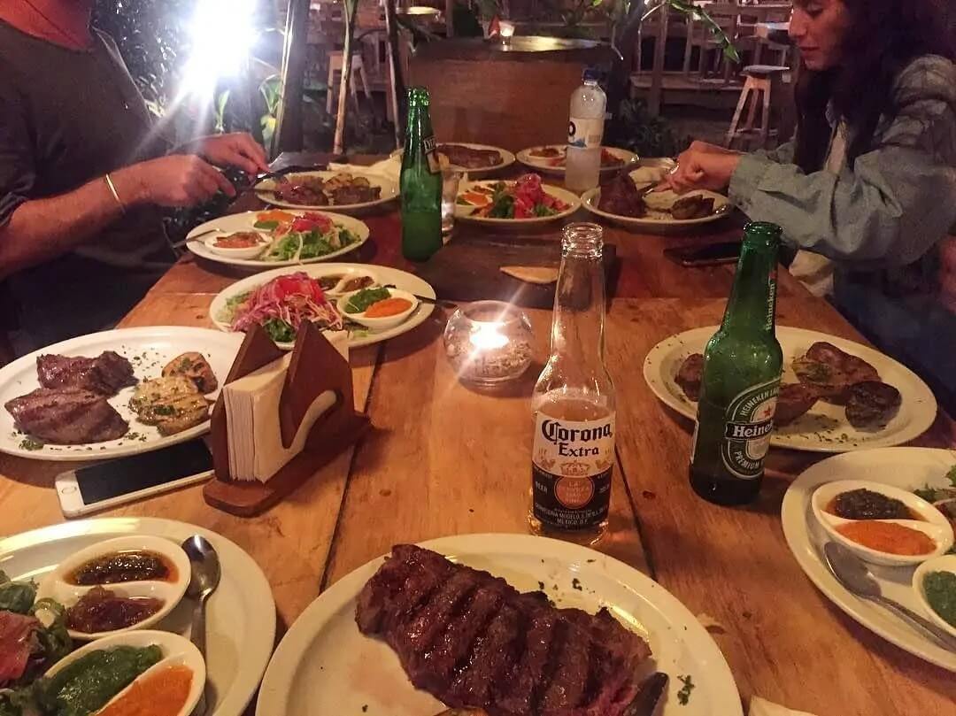 Beer and steak on a table with diners in the background.