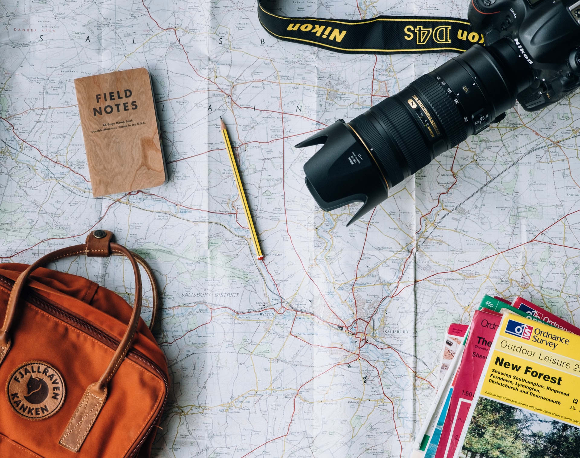 Camera, books, backpack, and a pencil laying on a map