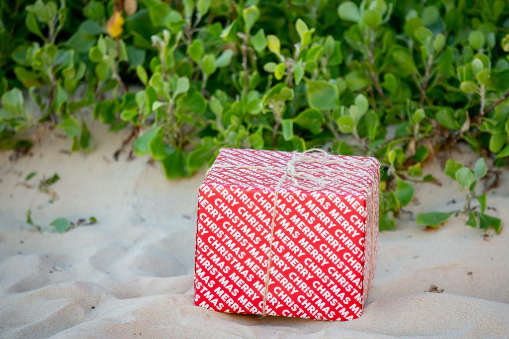 A red box with “Merry Christmas” wrapping paper sitting on a sandy beach