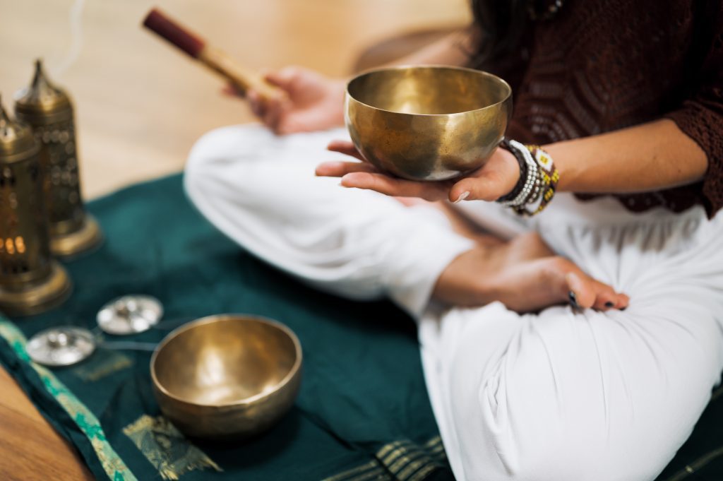Person sitting in half-lotus pose with singing bowls at a luxury yoga retreat
