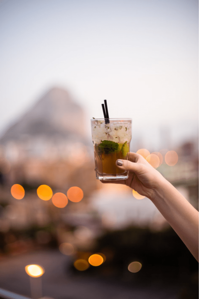A raised glass of a large mojito is raised at sunset