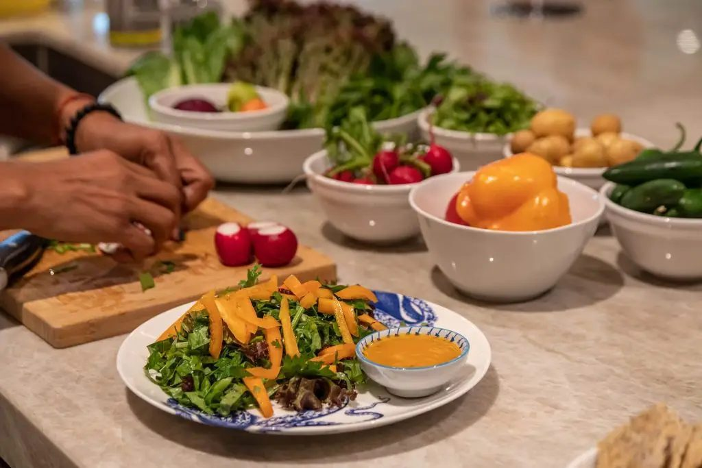 Plates and bowls of colorful produce and ingredients near a chef using a cutting board