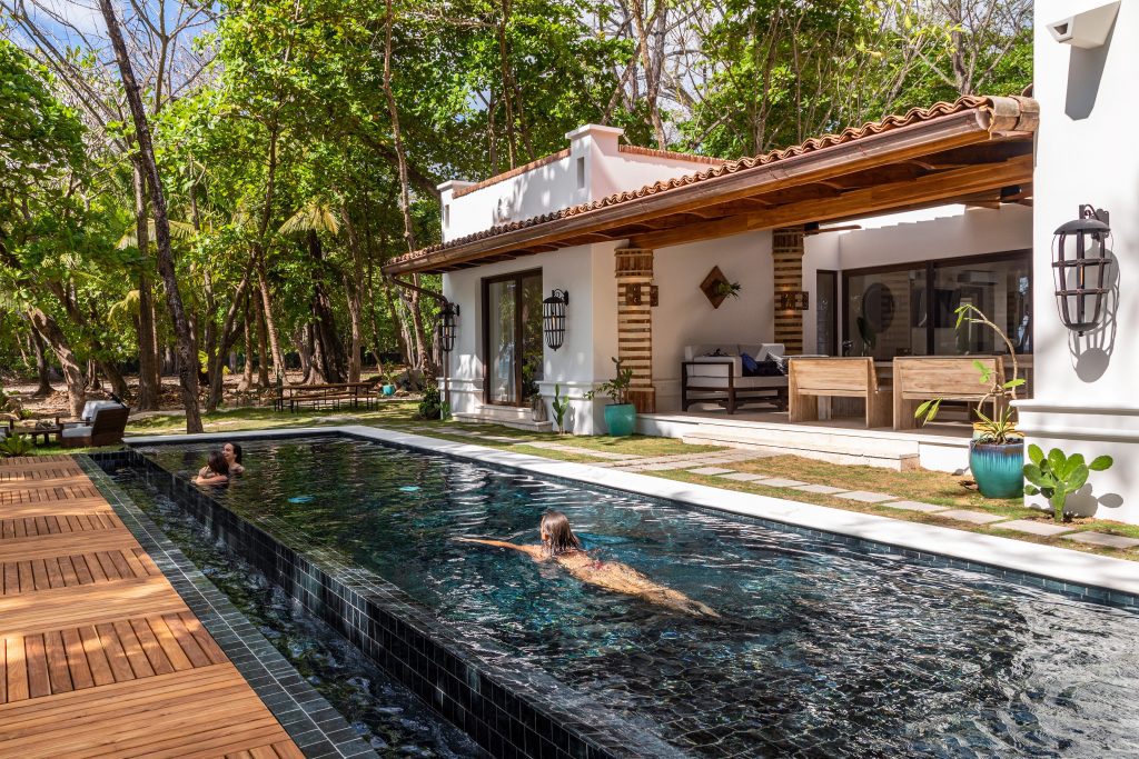 Group of friends swimming in the infinity pool at Casa Teresa Luxury Villas in Santa Teresa, Costa Rica surrounded by tropical forest and steps from the beach with open dining area