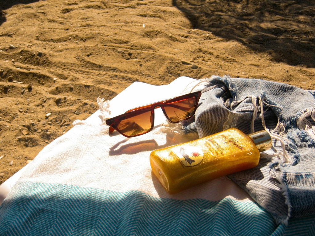 Sunglasses and a bottle of sunscreen on a towel at the beach