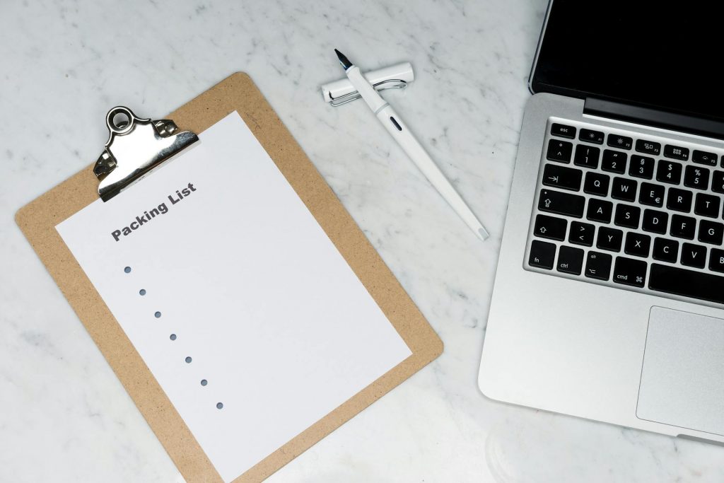 Clipboard with blank packing list on it beside a fountain pen and laptop