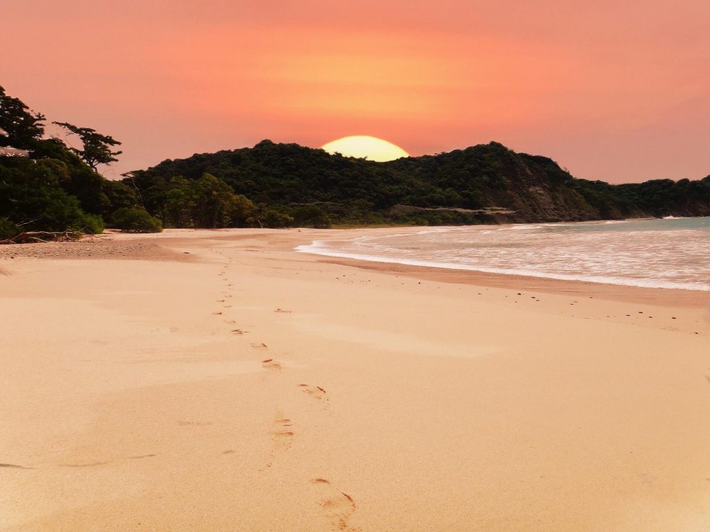 calm and remote beach at sunset with a large sun setting behind a bluff