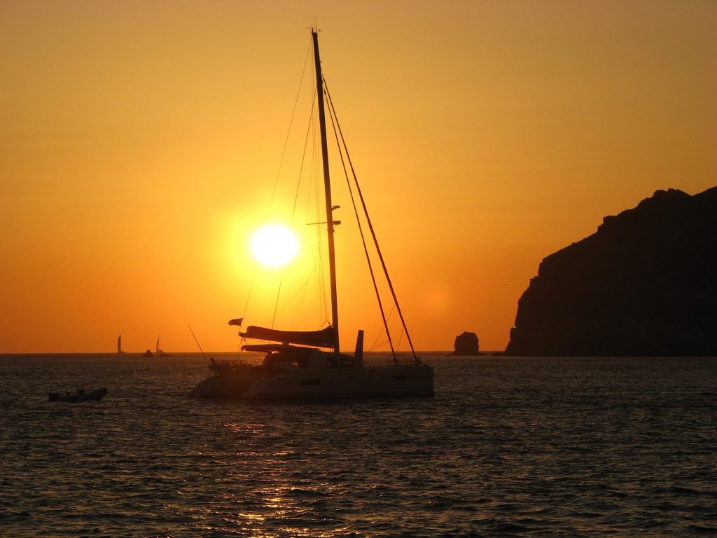The silhouette of a catamaran against the sunset, floating in balmy waters